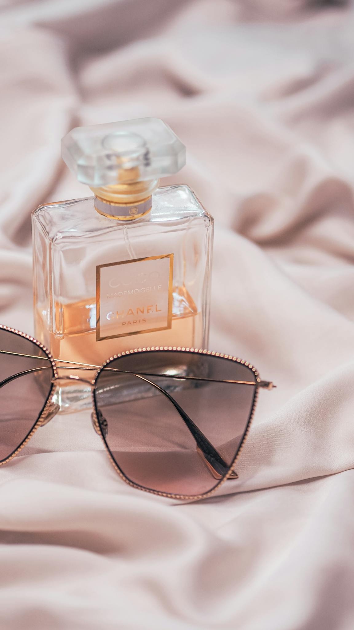 Chanel perfume with stylish sunglasses on soft satin fabric, exuding elegance.